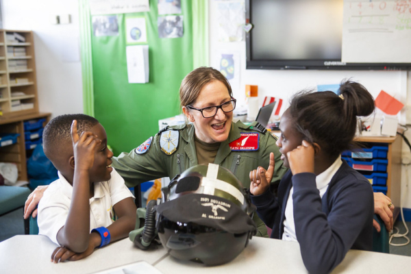 Female pilot in uniform talks with two excited students about aviation